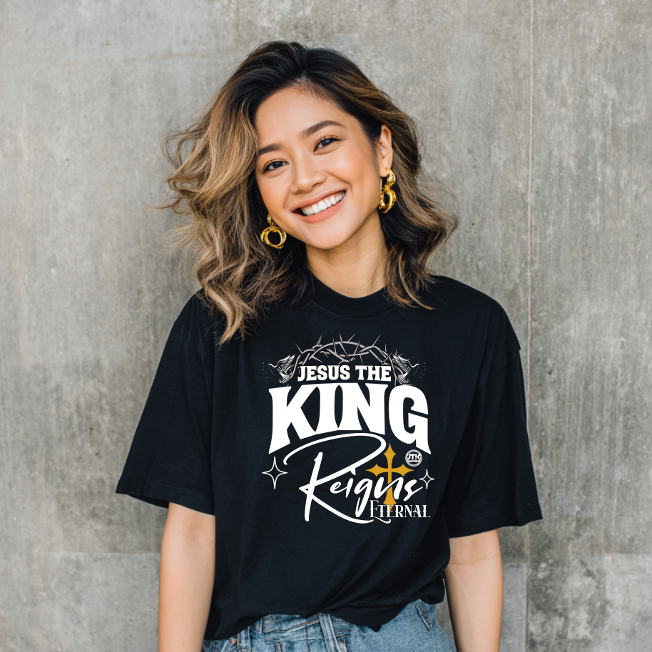 Woman wearing a black t-shirt with 'Jesus the King Reigns Eternal' text against a gray concrete wall.